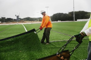 A worker lays a sheet of turf onto the Beach Chalet soccer fields.